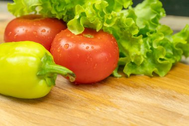 Su damlalı güzel, sulu sebzeler Biberler, domatesler, ahşap bir tahta üzerinde marul yaprakları