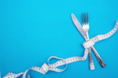 Çatal ve bıçak mezuraya sarılır. Kopya alanı olan mavi arkaplanda bir santimetre. Sağlık, kilo kaybı, diyet, uygun beslenme.