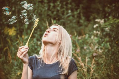 Genç, güzel sarışın kadın parkta sabun köpüğü üflüyor..