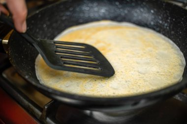 Kadının eli, tavada siyah spatula olan bir krepi yakın plan çekimde döndürür. Kahvaltı konsepti