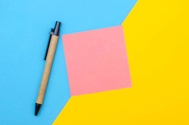 Pembe not kağıdı, sarı-mavi arkaplanlı kalem fotokopi alanı, üst görünüm