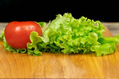 yeşil marul yaprakları, ahşap tahtada su damlaları olan domates, arka planda siyah arkaplan, kopyalama alanı