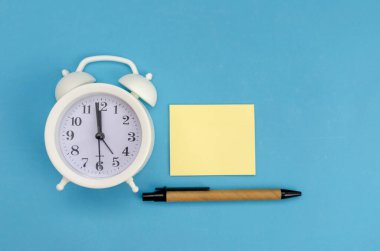 Sarı kayıt kağıdına sahip beyaz alarm saati, mavi arkaplanda kalem, kopyalama alanı
