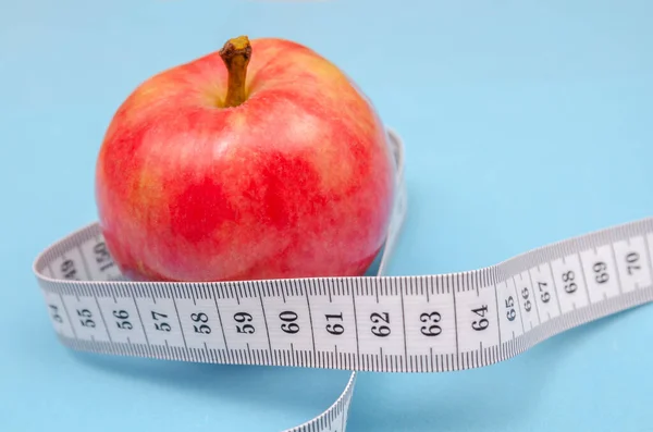 Red apple with a white centimeter close-up on a blue background. Healthy eating concept, calorie count and weight loss