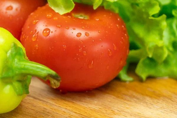 Su damlalı güzel, sulu sebzeler Biberler, domatesler, ahşap bir tahta üzerinde marul yaprakları