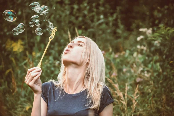 Genç, güzel sarışın kadın parkta sabun köpüğü üflüyor..