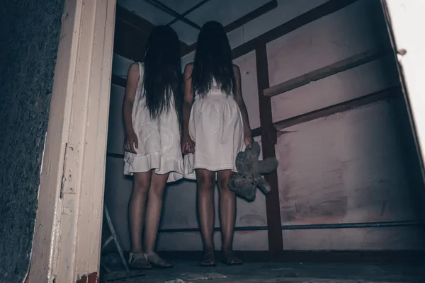 長い髪をした白いドレスを着た2人の女の子テディベアを手に持って暗い放棄された部屋に立って手を握ります 恐怖神秘主義という概念は — ストック写真