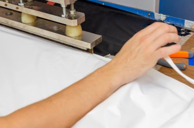 Erkeklerin elleri makinede PVC film ve kenar dikişler için çalışıyor. Gergin tavan üretimi için dükkan..