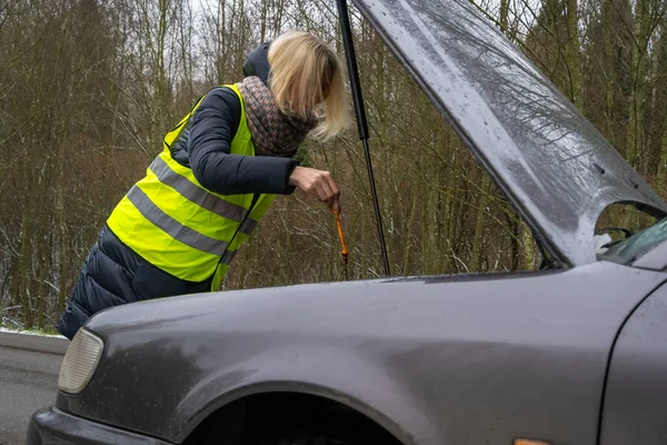 Młoda Blondynka Zimowej Kurtce Żółtej Kamizelce Sprawdza Poziom Oleju Silnikowego — Zdjęcie stockowe