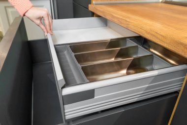 Kadının eli mutfak çekmecesini boş bir çatal bıçak tepsisiyle açıyor. İki çekmece yüksek bir cephenin arkasında saklı. Güzel modern mutfak.