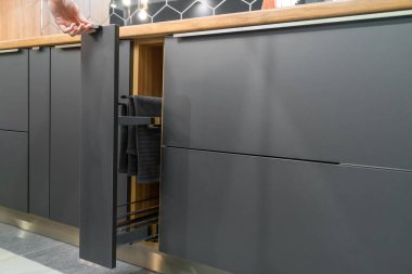 Kadının eli mutfakta havlu ve kavanozlar için bir çekmece açıyor. Gri, ahşap tonlarda modern güzel mutfak.