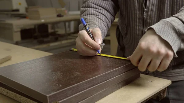 Close-up of a master in a furniture workshop marking out wooden tiles. Manufacture of furniture, shop of factory.