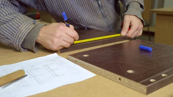 Close-up of a master in a furniture workshop marking out wooden tiles. Manufacture of furniture, shop of factory.