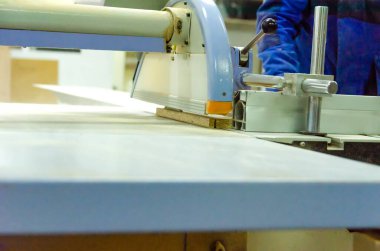 Erkek çalışan ahşap işleme için bir format kesme makinesinin arkasında duruyor. Marangoz atölyesinde ahşap işçiliği.