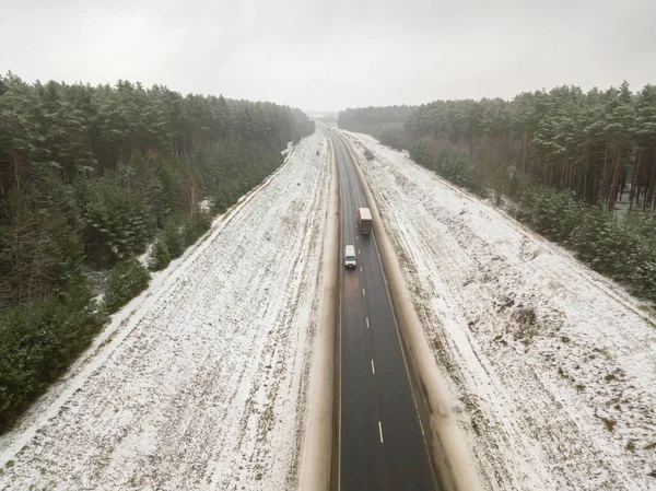 Road with cars in the middle of the forest on a snowy winter day, view from a drone