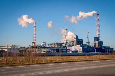 Fabrikada, güneşli bir günde mavi gökyüzüne karşı kocaman duman bulutları olan borular, yoldan çekilmiş fotoğraflar. Ekoloji kavramı, çevre kirliliği
