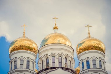 Altın kubbeler, Doğu Ortodoks haçları olan kubbeler beyaz bir kilisede bulutlu mavi bir gökyüzüne karşı.