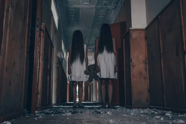 長い髪の白いドレスを着た2人の女の子が放棄された建物の不気味な廊下の真ん中でテディベアを一緒に持っています 恐怖神秘主義という概念は — ストック写真