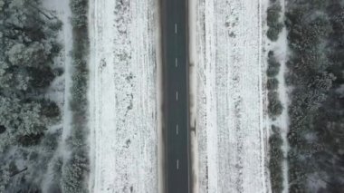 Karla kaplı bir yol ve kış ormanı boyunca insansız hava aracı hareketi.