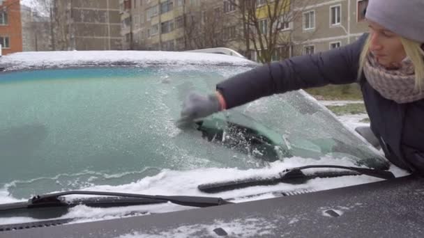 Mujer raspa el hielo del parabrisas de su coche después de un largo estacionamiento. — Vídeos de Stock