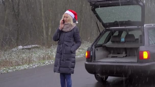 Mulher em Santa Claus chapéu chamadas no smartphone, carro quebrado. — Vídeo de Stock