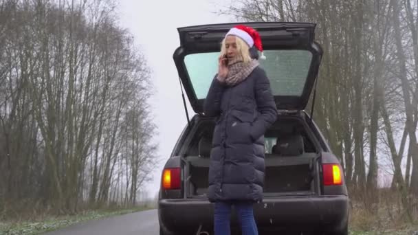 Mujer en Santa Claus sombrero llamadas en el teléfono inteligente, coche roto. — Vídeos de Stock