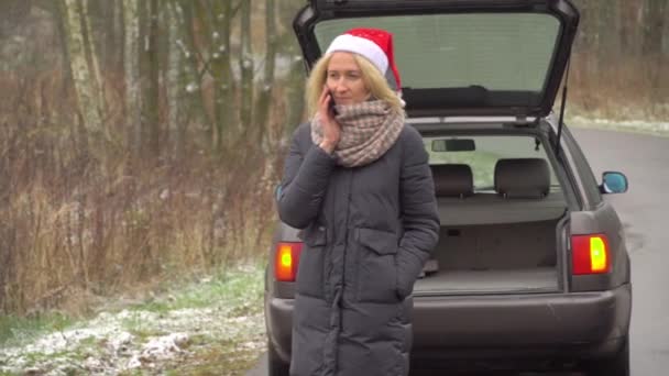 Mujer en Santa Claus sombrero llamadas en el teléfono inteligente, coche roto. — Vídeo de stock