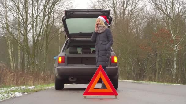 Mujer en Santa Claus sombrero llamadas en el teléfono inteligente, coche roto. — Vídeo de stock