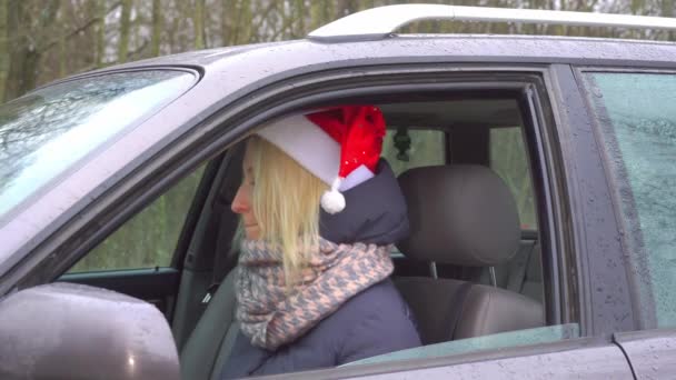 En kvinna i tomte hatt sitter i en bil, dansar och sjunger. — Stockvideo