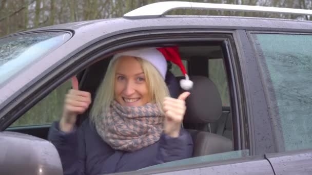 Vrouw in de kerstman hoed zit in de auto, overeind houden OK teken — Stockvideo
