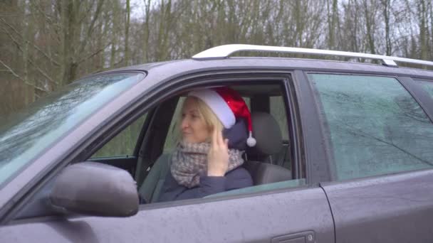 Mujer en Santa Claus sombrero está sentado en el coche, sosteniendo "OK" signo" — Vídeos de Stock