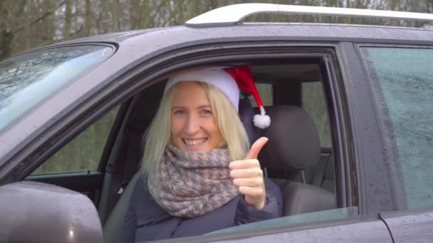 Vrouw in de kerstman hoed zit in de auto, overeind houden OK teken — Stockvideo