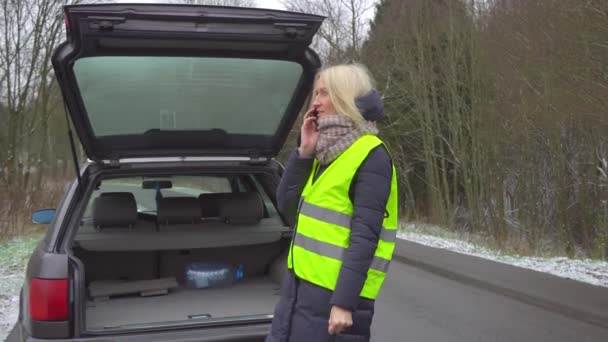 Une femme appelle sur son smartphone alors qu'elle se tient près d'une voiture cassée. — Video