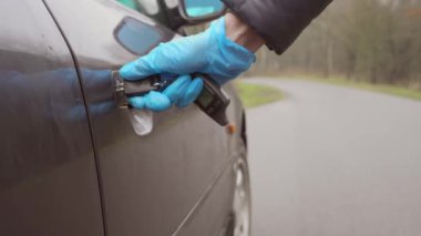 Tek kullanımlık eldivenler giymiş bir kadının eli arabanın kapısını kapatır ve kilidi açar..