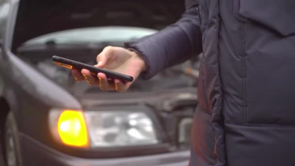 Detailní záběr ruky pomocí telefonu na pozadí vozu s blikajícím alarm