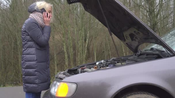 Una mujer llama a su teléfono inteligente mientras está de pie junto a un coche roto. — Vídeo de stock