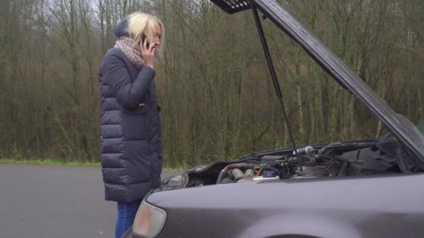 Жінка дзвонить на свій смартфон, стоячи на зламаній машині . — стокове відео