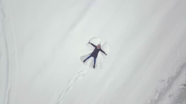 Una donna giace sulla neve e disegna un angelo. Sparatoria da un drone. — Video Stock