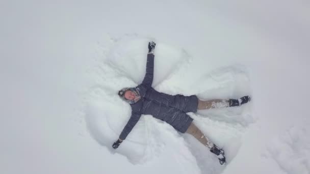 Gondtalan fiatal nő lengeti a karját és a lábát egy hóviharban. Angyal — Stock videók