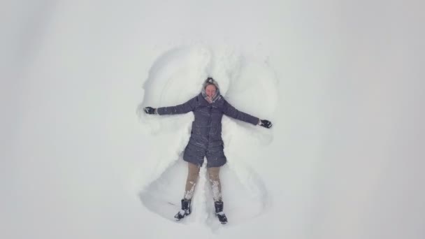 Egy nő fekszik a hóban, és rajzol egy angyalt. Lövöldözés egy drónról. — Stock videók