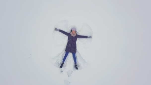 En kvinna ligger på snön och ritar en ängel. Skjuta från en drönare. — Stockvideo
