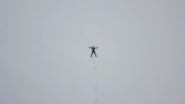 Eine Frau liegt auf dem Schnee und zeichnet einen Engel. Schießen aus einer Drohne. — Stockvideo