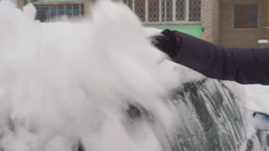 Bir kadın arabayı bir fırçayla kardan temizliyor..