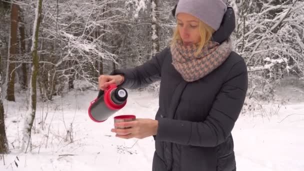 Eine Frau gießt Tee oder Kaffee aus einer Thermoskanne in eine Tasse. Wald, Winter. — Stockvideo