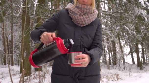 Une femme verse du thé ou du café d'un thermos dans une tasse. Forêt, hiver. — Video