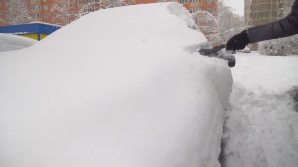 Una mujer limpia el coche de la nieve con un cepillo. — Vídeos de Stock