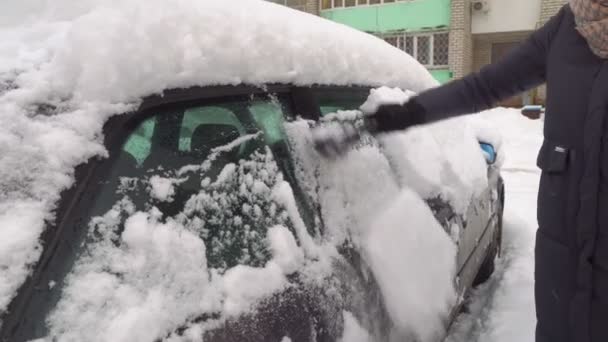 Una mujer limpia el coche de la nieve con un cepillo. — Vídeos de Stock