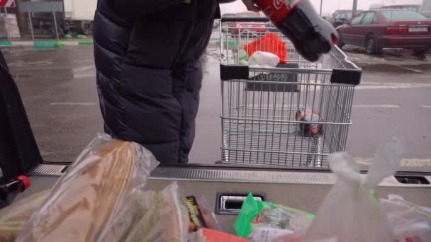 Een jonge vrouw zet eten in de kofferbak van een auto op de parkeerplaats van een supermarkt. — Stockvideo