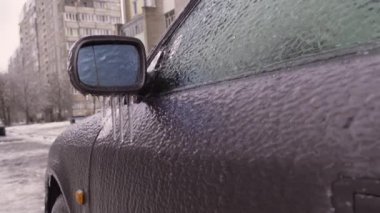 Buzlu bir yağmurdan sonra buzlu bir araba. Aynada ve arabanın kemerlerinde buz saçakları asılı..