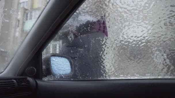 Mujer raspa el hielo del parabrisas de su coche después de un largo estacionamiento. — Vídeos de Stock